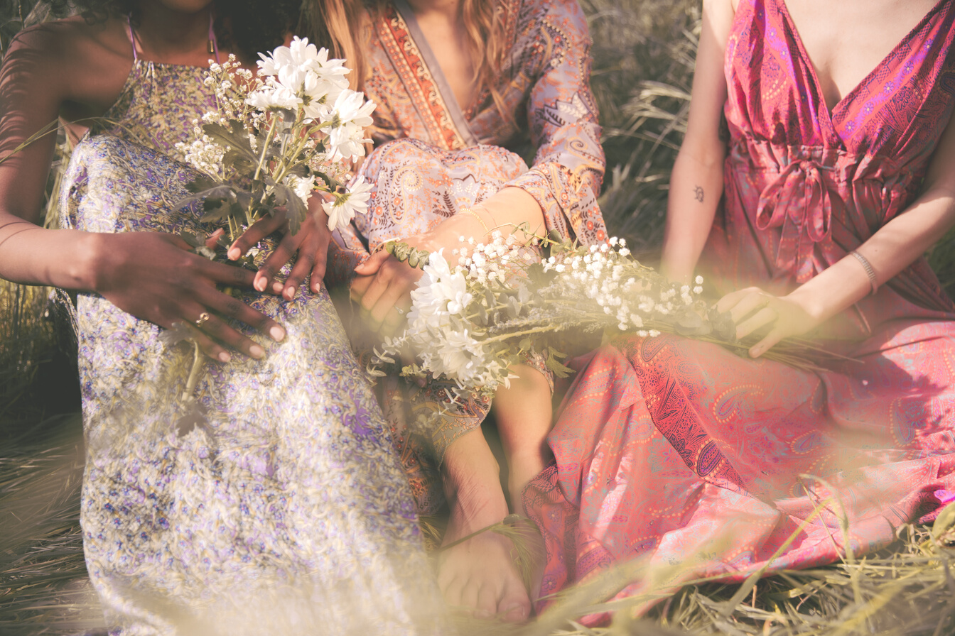 Three Female Friends with Flowers Sitting on Grass
